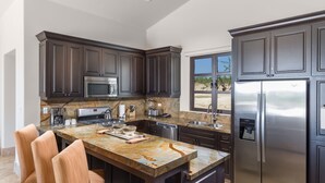 A modern kitchen with dark cabinetry, a stainless steel refrigerator, a built-in microwave, and a marble countertop.