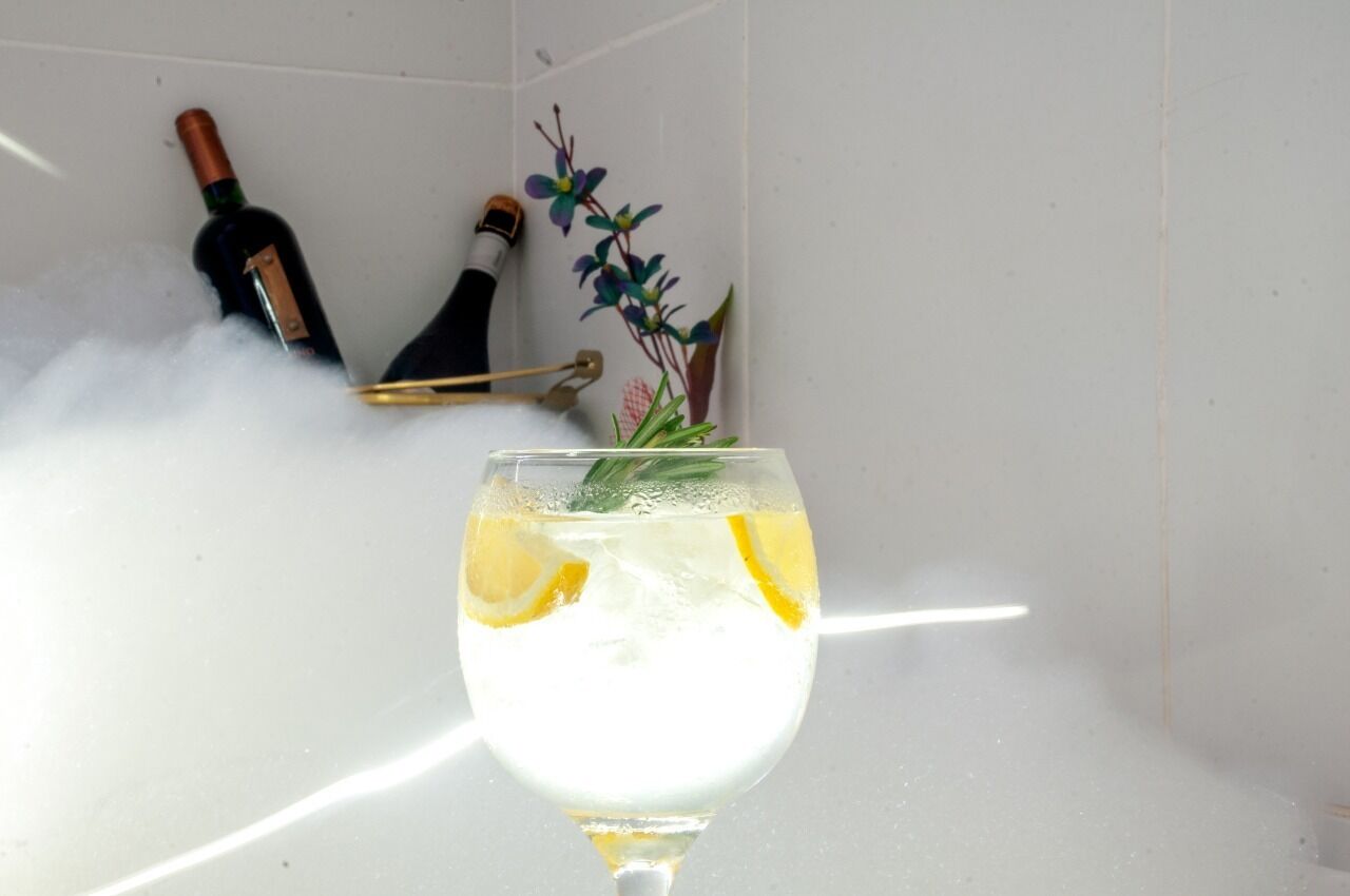 A glass of white beverage with lemon slices, a bottle of wine, and a decorative plant in a bathroom setting.