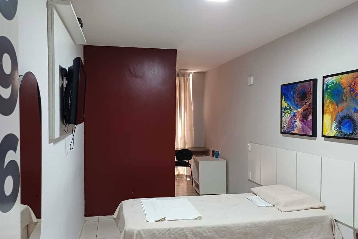A hotel room with a bed, a TV, and two paintings on the wall.