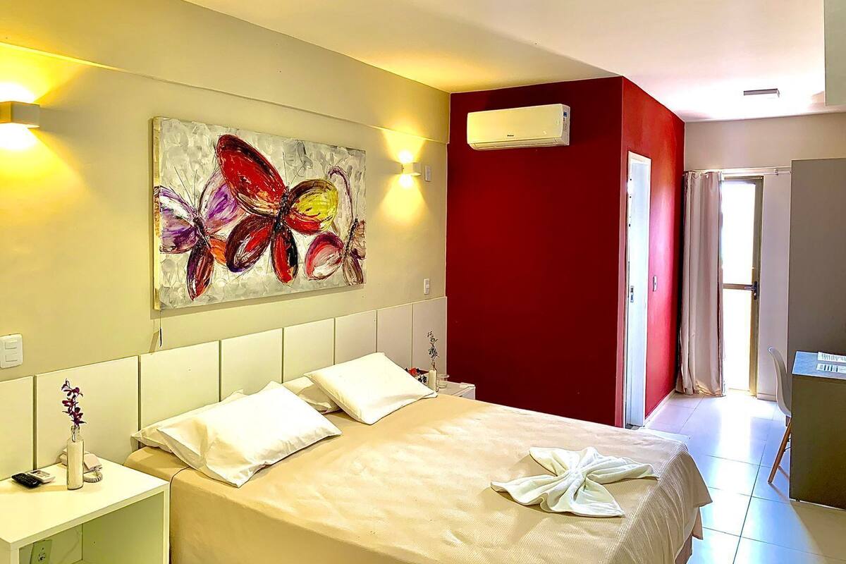 A hotel room with a bed, a painting, an air conditioner, and a bathroom visible through an open door.
