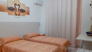 A room with two beds, a white desk, a wall-mounted air conditioner, and a curtain. - Giosy (Portopalo di Capo Passero)