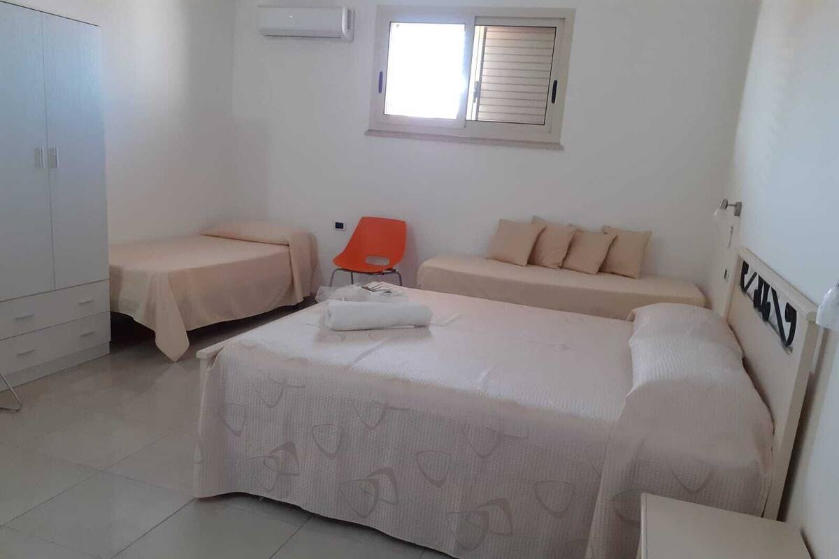 A bedroom with two single beds, a sofa bed, a wardrobe, and a window with blinds.