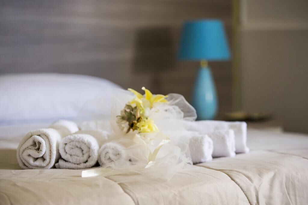 A neatly made bed with rolled white towels and a bouquet of flowers.