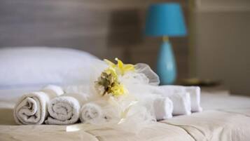 A neatly made bed with rolled white towels and a bouquet of flowers.