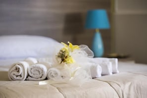 A neatly made bed with rolled white towels and a bouquet of flowers. - Giosy (Portopalo di Capo Passero)