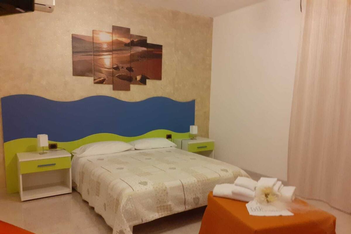 A hotel room with a bed, a nightstand, a table with a towel, and a wall art piece.