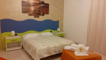A hotel room with a bed, a nightstand, a table with a towel, and a wall art piece.