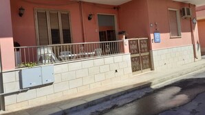 A pink building with a balcony, a gated entrance, and a small window with shutters. - Giosy (Portopalo di Capo Passero)