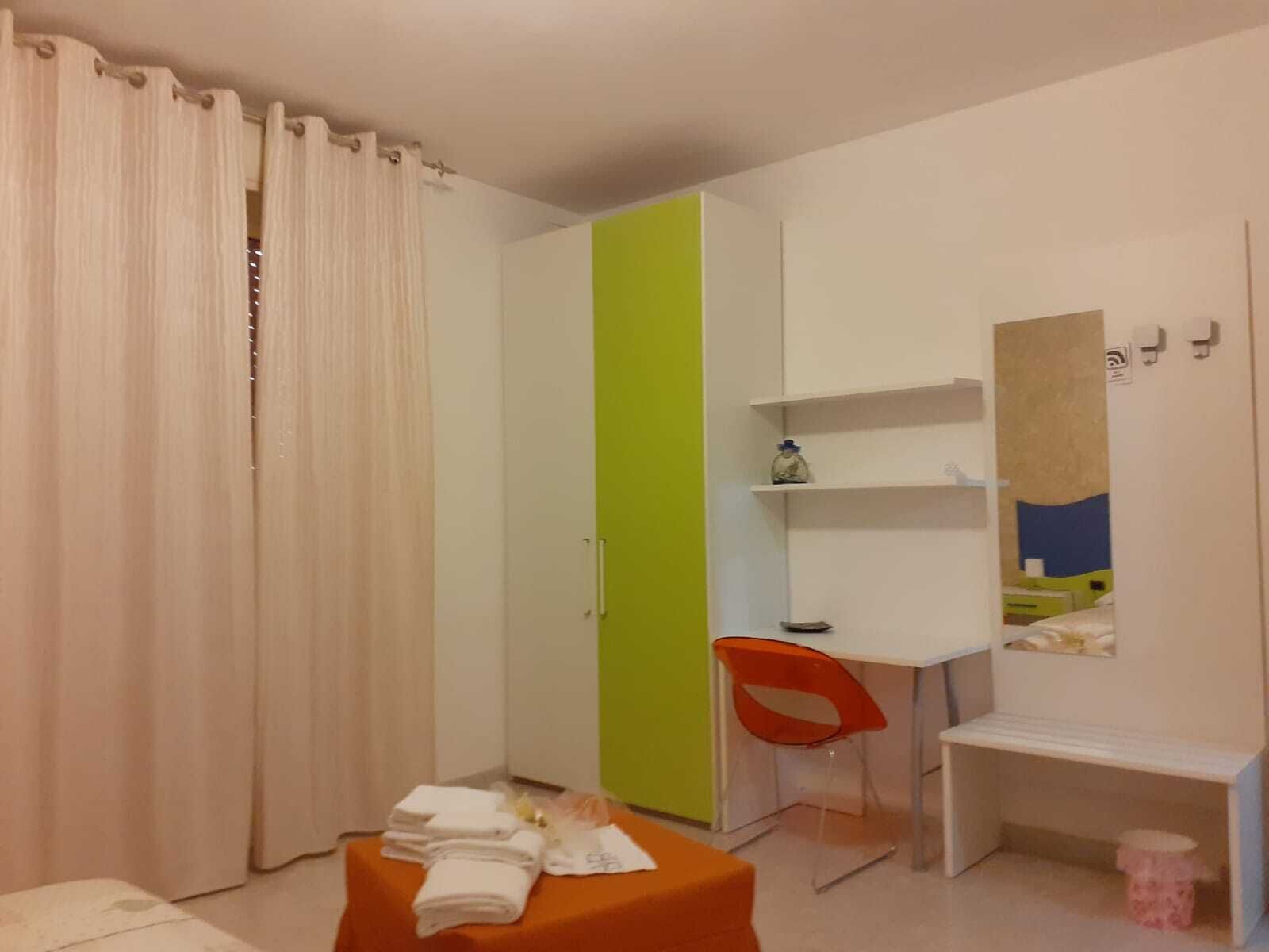 A hotel room with a bed, a desk, a chair, a wardrobe, and a mirror.
