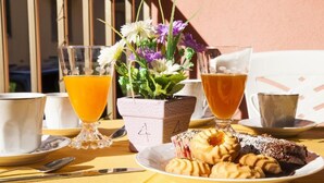 A breakfast setting with a plate of pastries, two glasses of orange juice, and a floral centerpiece on a yellow tablecloth. - Giosy (Portopalo di Capo Passero)