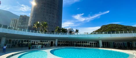 A modern building with a pool area, featuring a large circular pool and a tall skyscraper in the background.