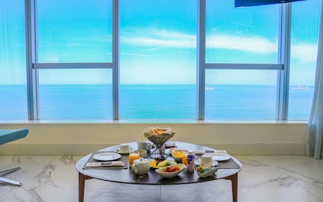 A breakfast table with various dishes and a view of the sea through large windows.