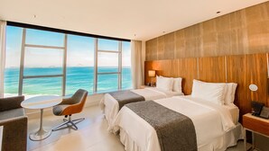 A hotel room with two beds, a small table, a chair, and a view of the ocean. - Hotel Nacional Rio de Janeiro OFICIAL (Rio de Janeiro)