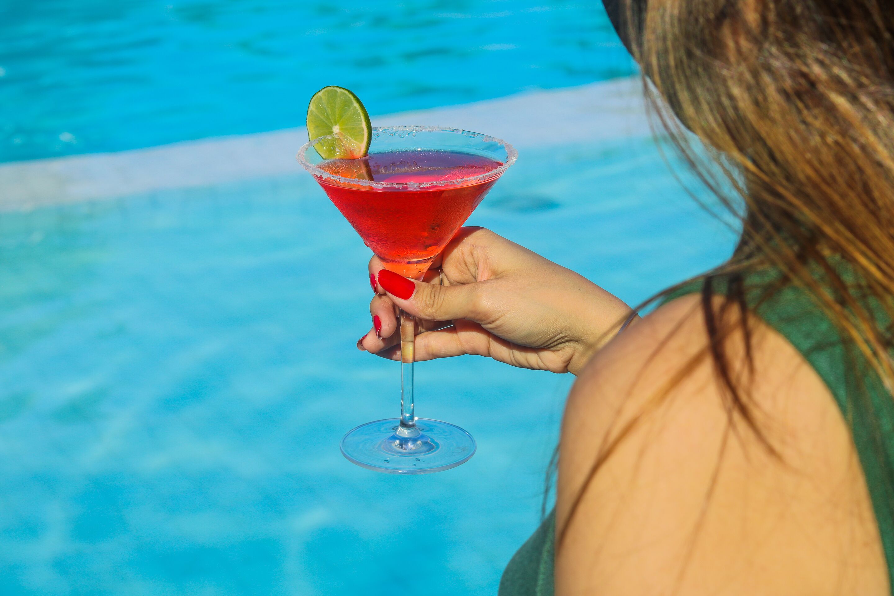 Una persona sosteniendo un cóctel con una rodaja de limón, junto a una piscina.