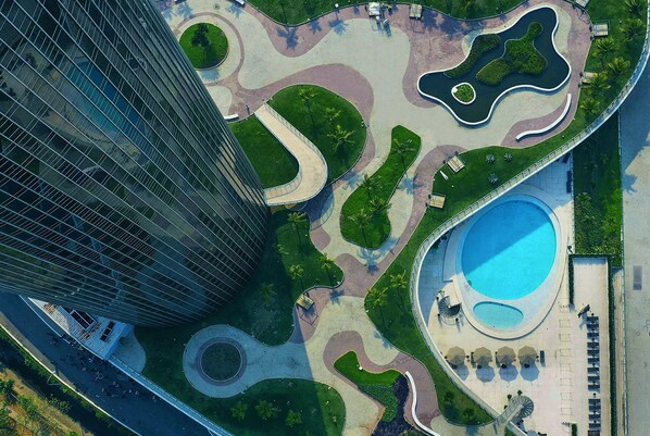 Vista aérea de una zona urbana moderna con un edificio grande, un parque circular con piscina y una carretera serpenteante.