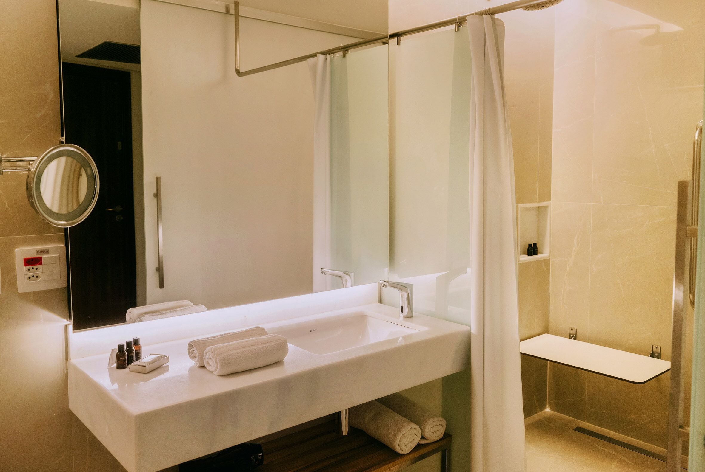 A modern bathroom with a white sink, a mirror, and a shower area.