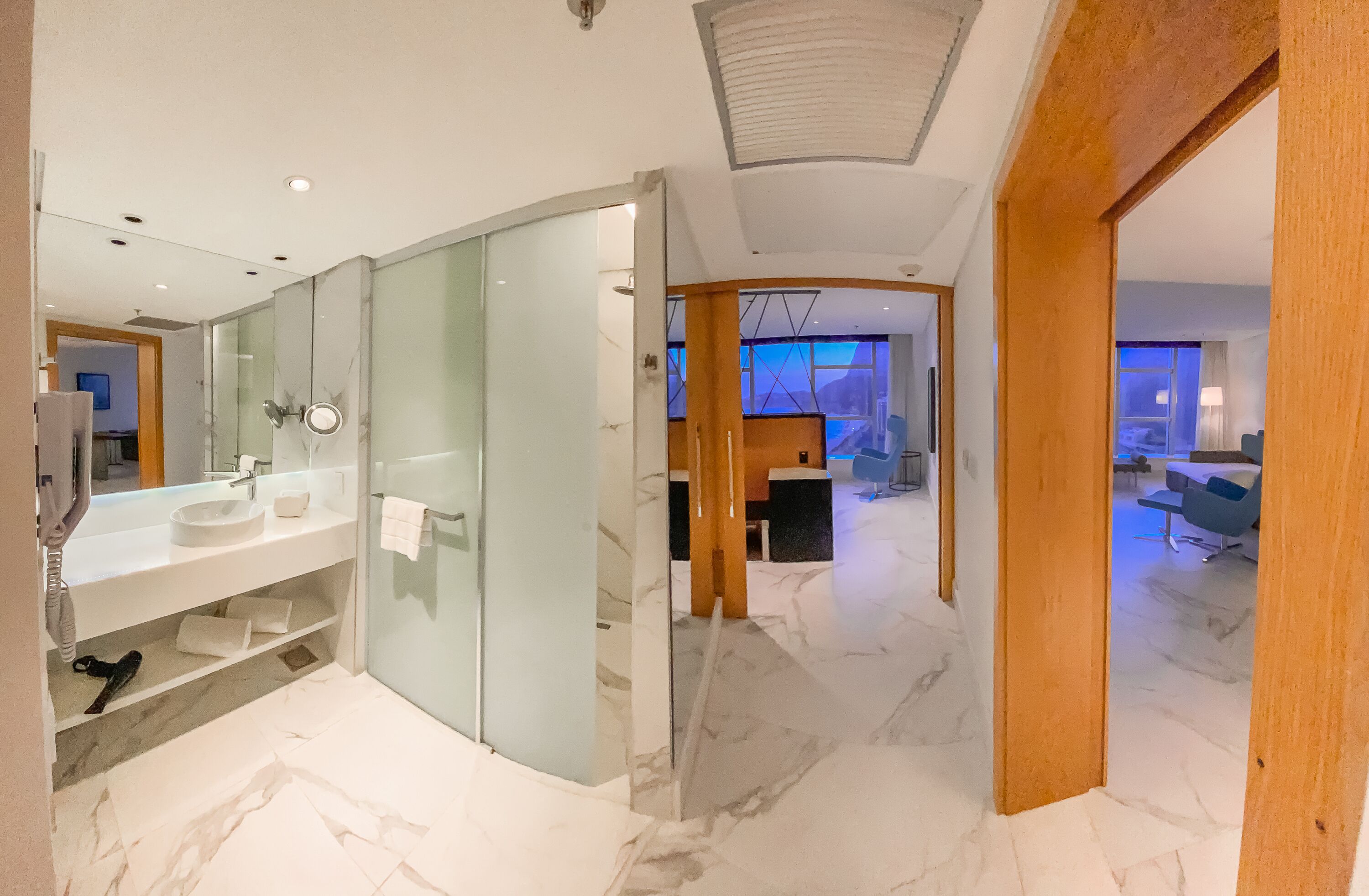 Un baño moderno con separador de vidrio, un espejo grande y suelo de mármol.
