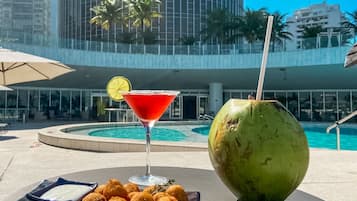 A poolside setting with a martini glass, a plate of fried balls, and a coconut.