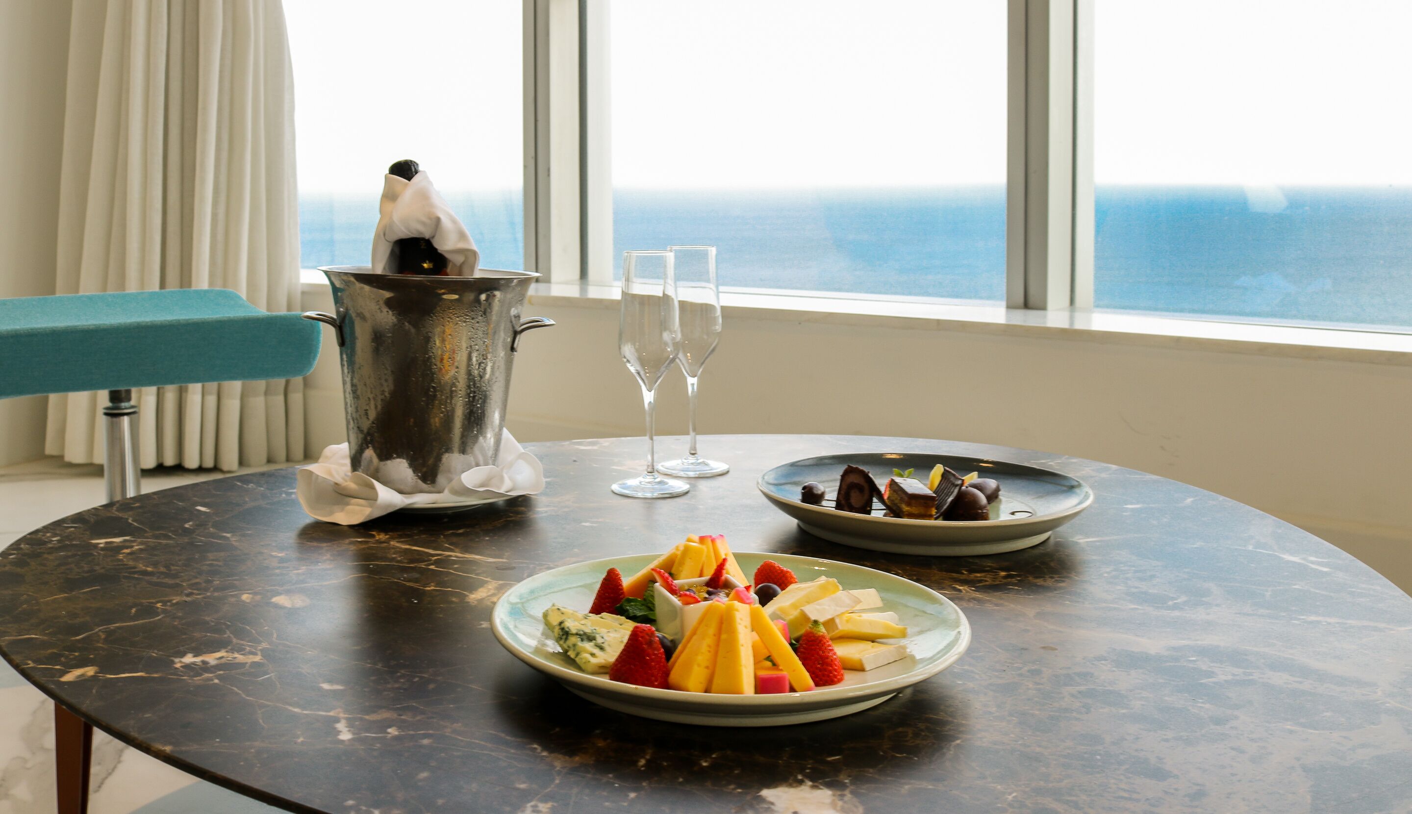 Uma mesa com um prato de frutas, uma fatia de sobremesa e uma bebida quente em uma chaleira.