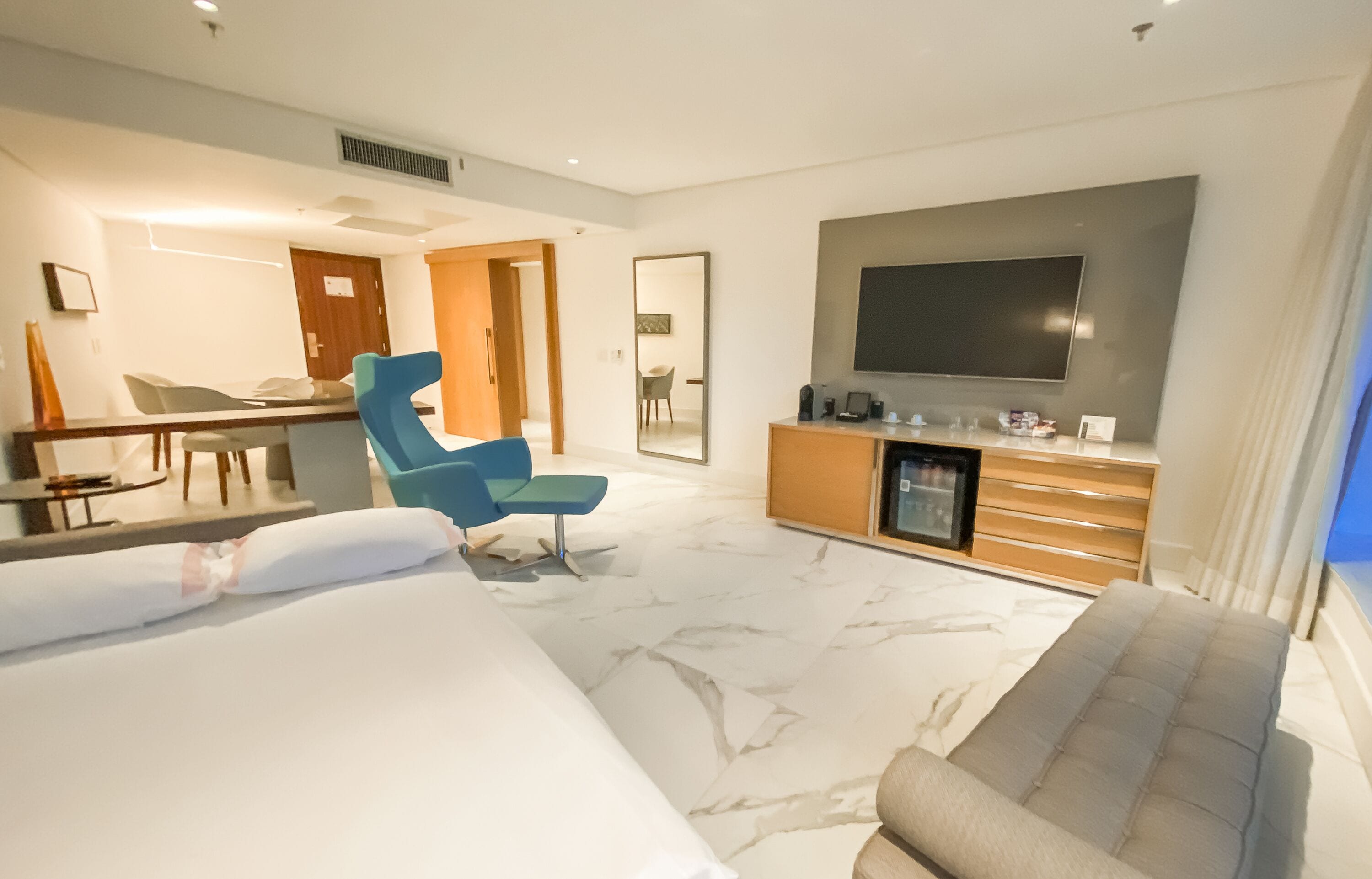 Una habitación de hotel moderna con una cama grande, un sillón azul, un televisor y un minibar.