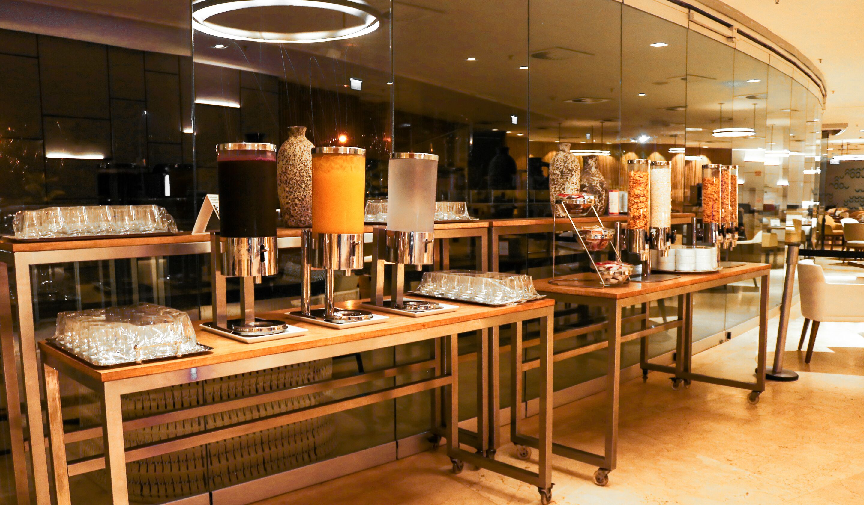 Uma área de buffet com diversos distribuidores de alimentos e uma vitrine de vidro.
