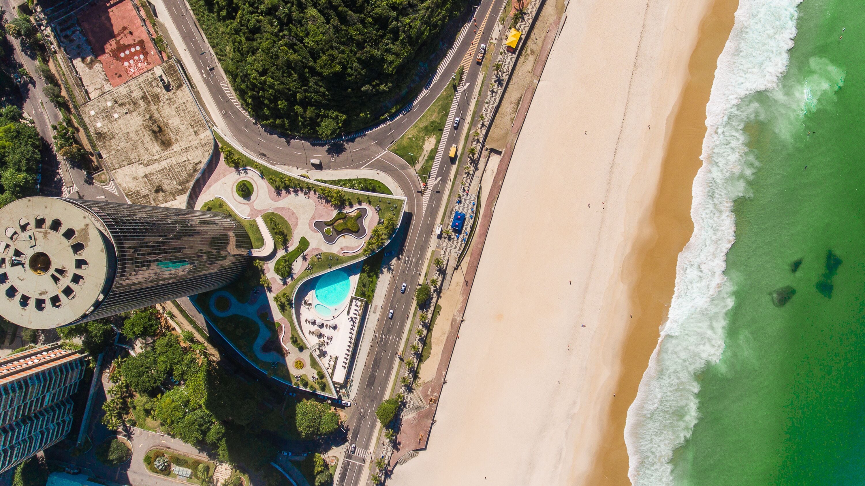 An aerial view of a coastal area with a beach, a roundabout, and a tall building with a circular observation deck.