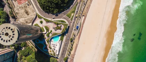 An aerial view of a coastal area with a beach, a roundabout, and a tall building with a circular observation deck.