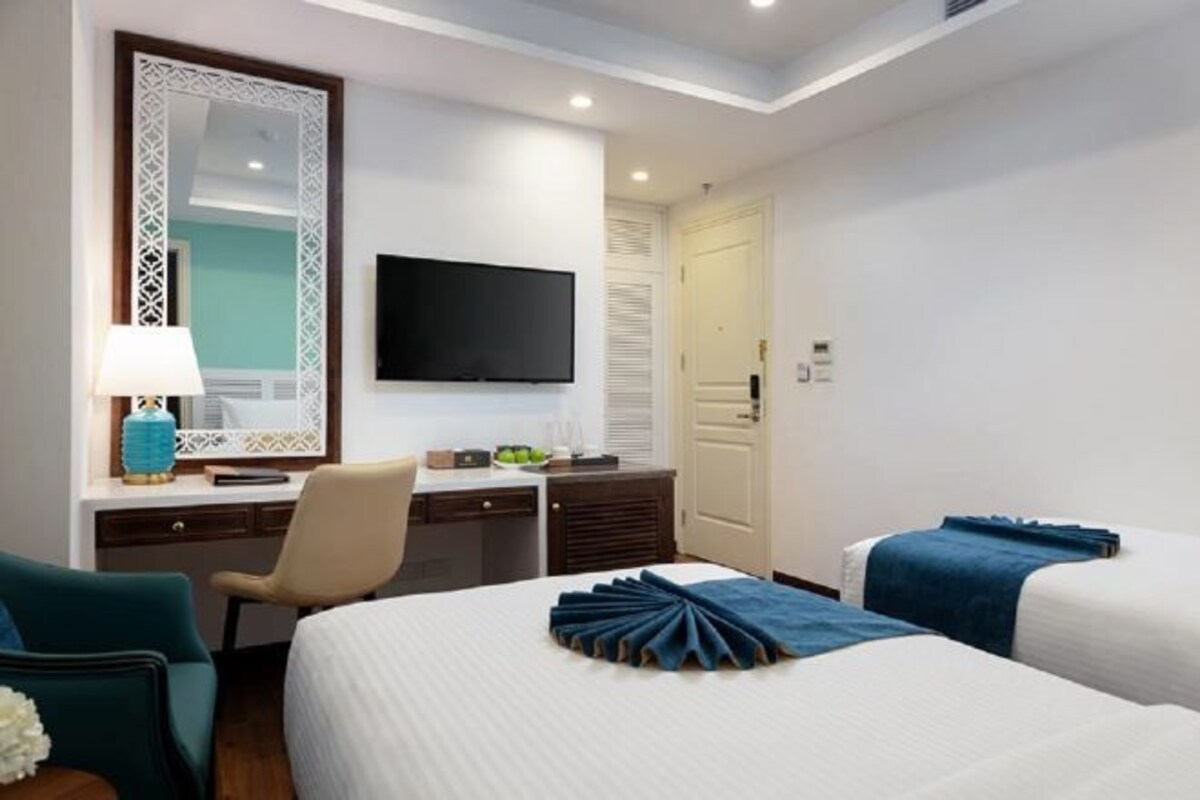 A hotel room with a bed, a desk with a chair, a television, and a door.