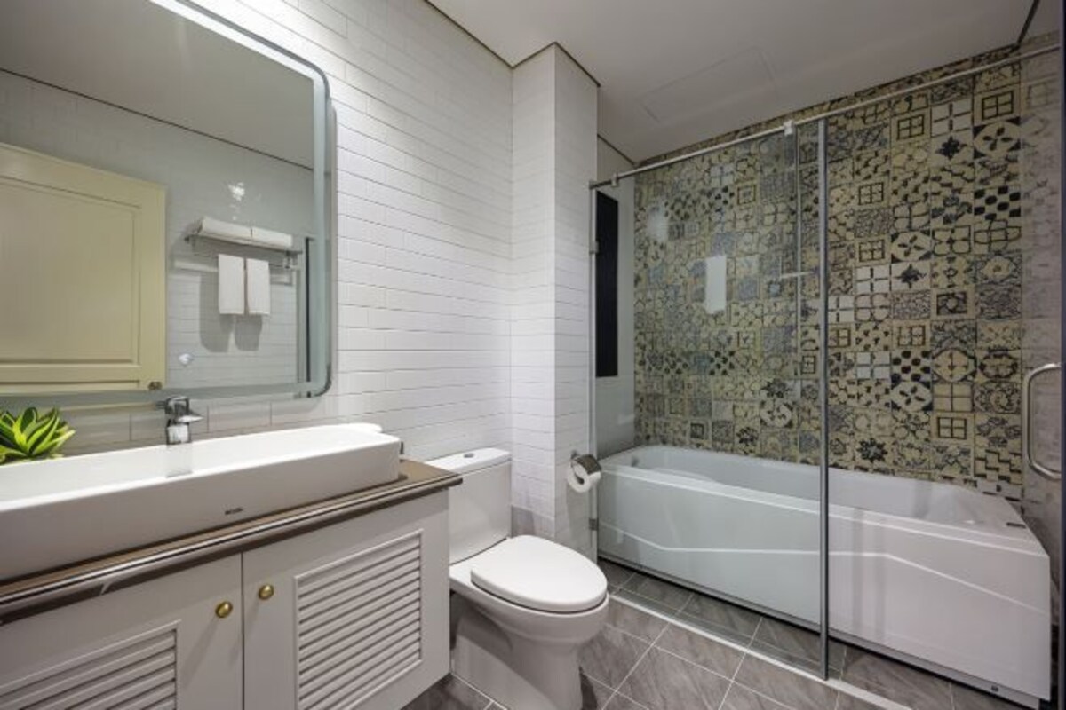 A modern bathroom with a white vanity, a toilet, a glass-enclosed shower, and a patterned tile wall.