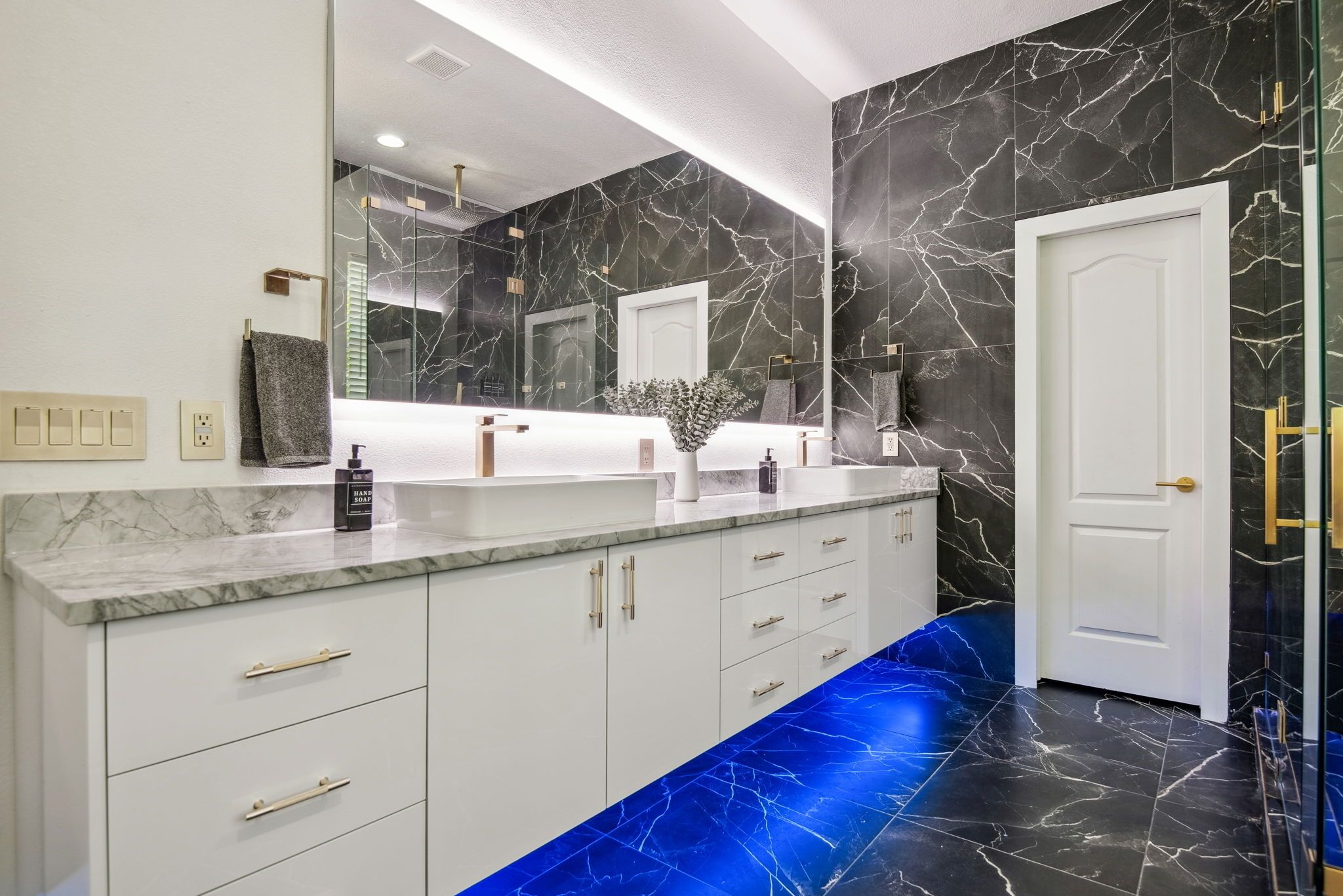 Un baño moderno con tocador de mármol, un espejo grande y piso cubierto de azulejos azules.