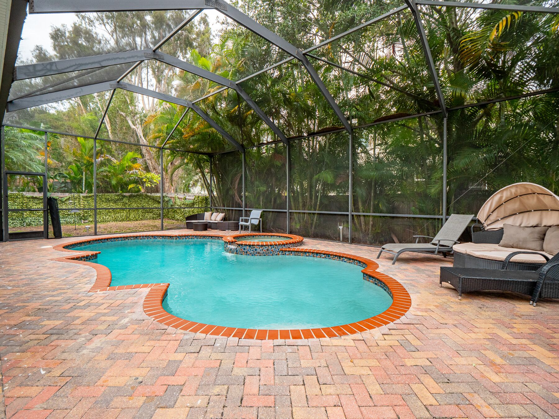 Una piscina techada con borde de ladrillo, rodeada de sillas de descanso y una estructura de pérgola.