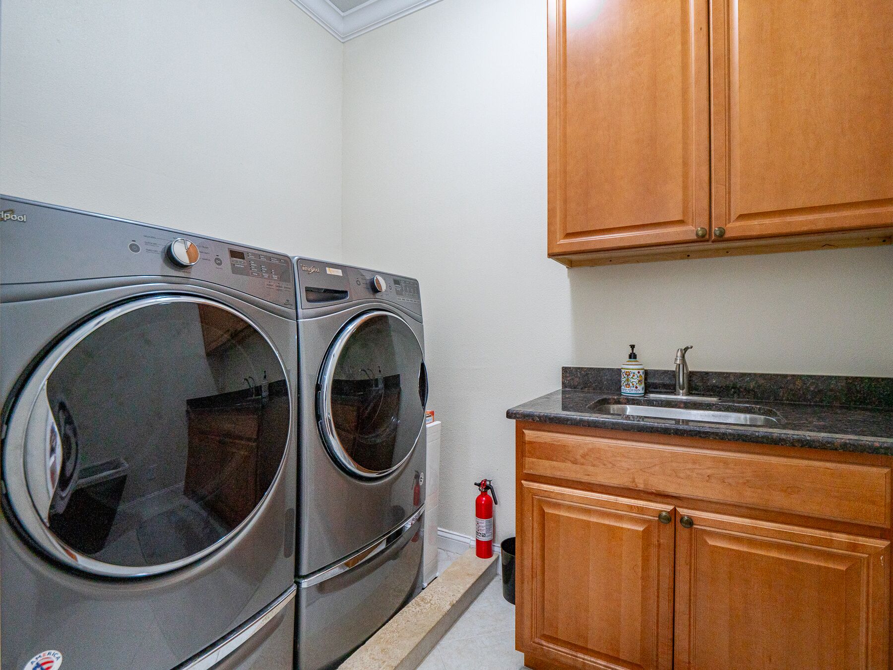 A laundry room with two front-loading washing machines, a sink, and wooden cabinets.