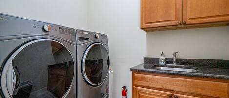 A laundry room with two front-loading washing machines, a sink, and wooden cabinets.
