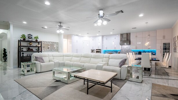 A modern living room with a sectional sofa, glass coffee table, and a dining area with white chairs. - ⭐️S. Tampa Mansion🔥Heated Pool+Spa🎬Movie Theater Chef’s Kitchen 5000sqft (Tampa)
