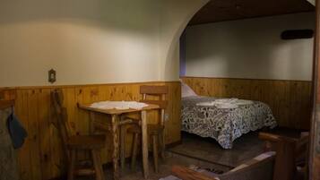Een gezellige kamer met een houten tafel, twee stoelen, een bed met een decoratieve spreidek en een gewelfde plafond.