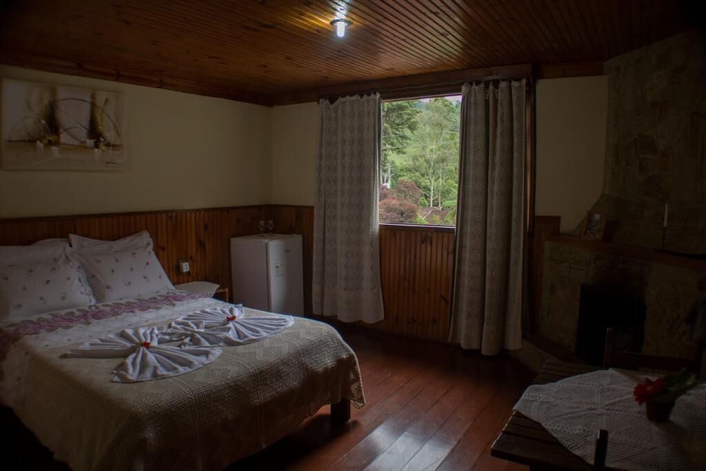 A cozy room with a wooden ceiling, a bed with a floral bedspread, a small table with a vase, and a stone fireplace.
