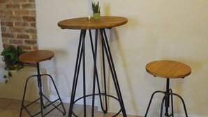 Una habitación con tres taburetes, una mesa redonda, una pared de ladrillo y dos hojas enmarcadas en la pared.