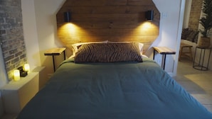 Un dormitorio con cabecera de madera, un cojín estampado con diseño de cebra y dos mesitas de noche con velas.