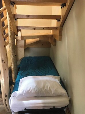 Een stapelbed met een blauwe matras en witte kussens, houten balken en een ladder.
