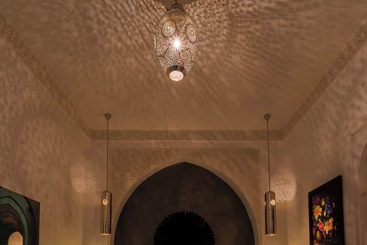 Quarto com uma cama grande, duas mesas de cabeceira, um lustre e um arco na parede.