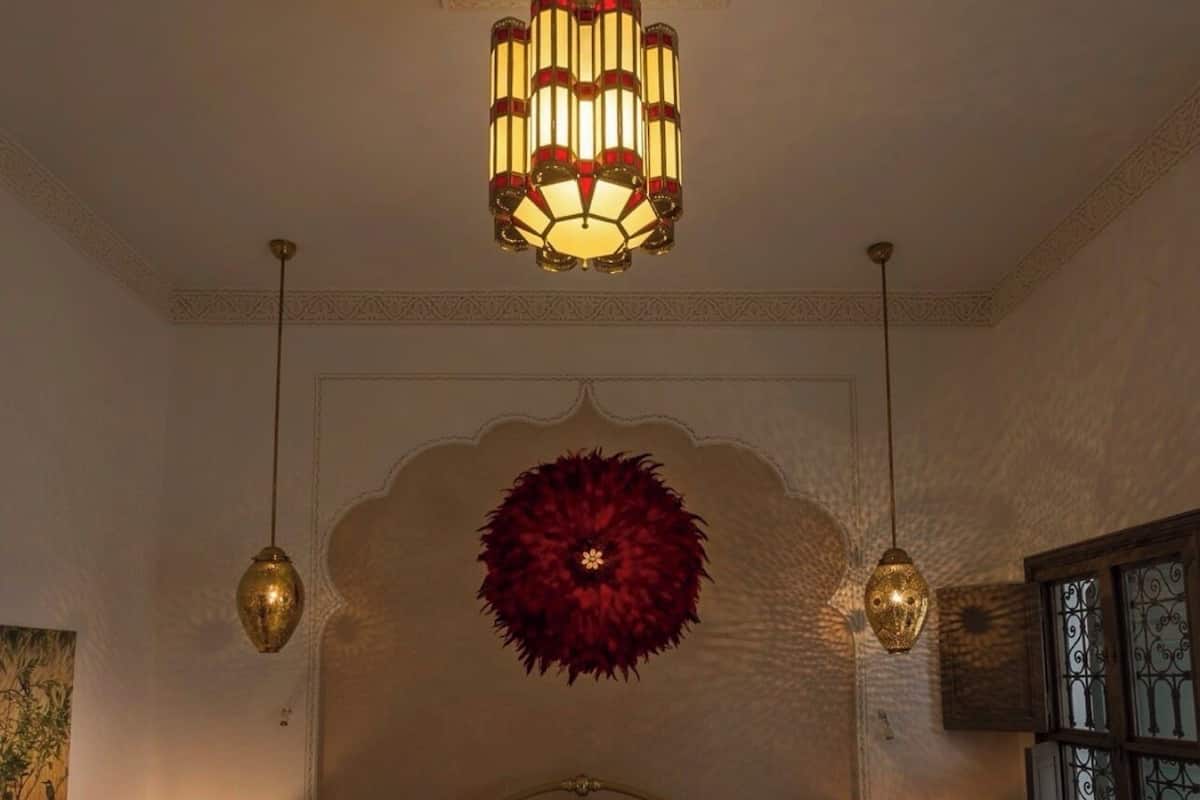 Quarto com uma cama, duas luminárias de cabeceira, um objeto decorativo na parede e um lustre.