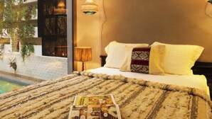 A bedroom with a bed, a magazine on the bed, a lamp, and a view of a pool and greenery outside. - Riad Lumière (Marrakech)