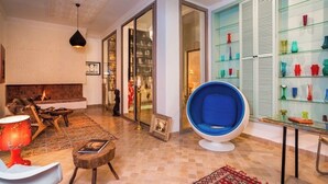 A living room with a fireplace, a blue chair, and a glass display of colorful vases. - Riad Lumière (Marrakech)
