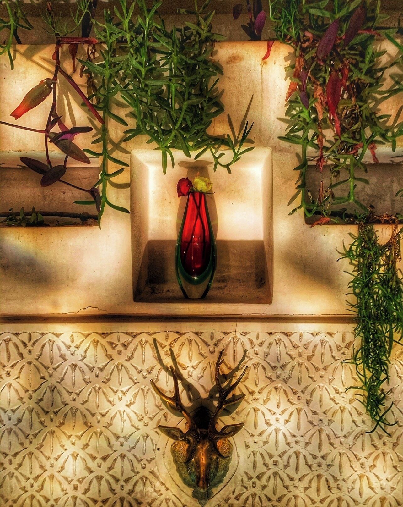 A decorative shelf with a vase containing flowers, surrounded by greenery.
