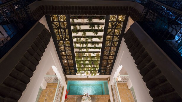 A view from a balcony overlooking a pool with a table and chairs, surrounded by ornate railings and a patterned floor. - Riad Lumière (Marrakech)
