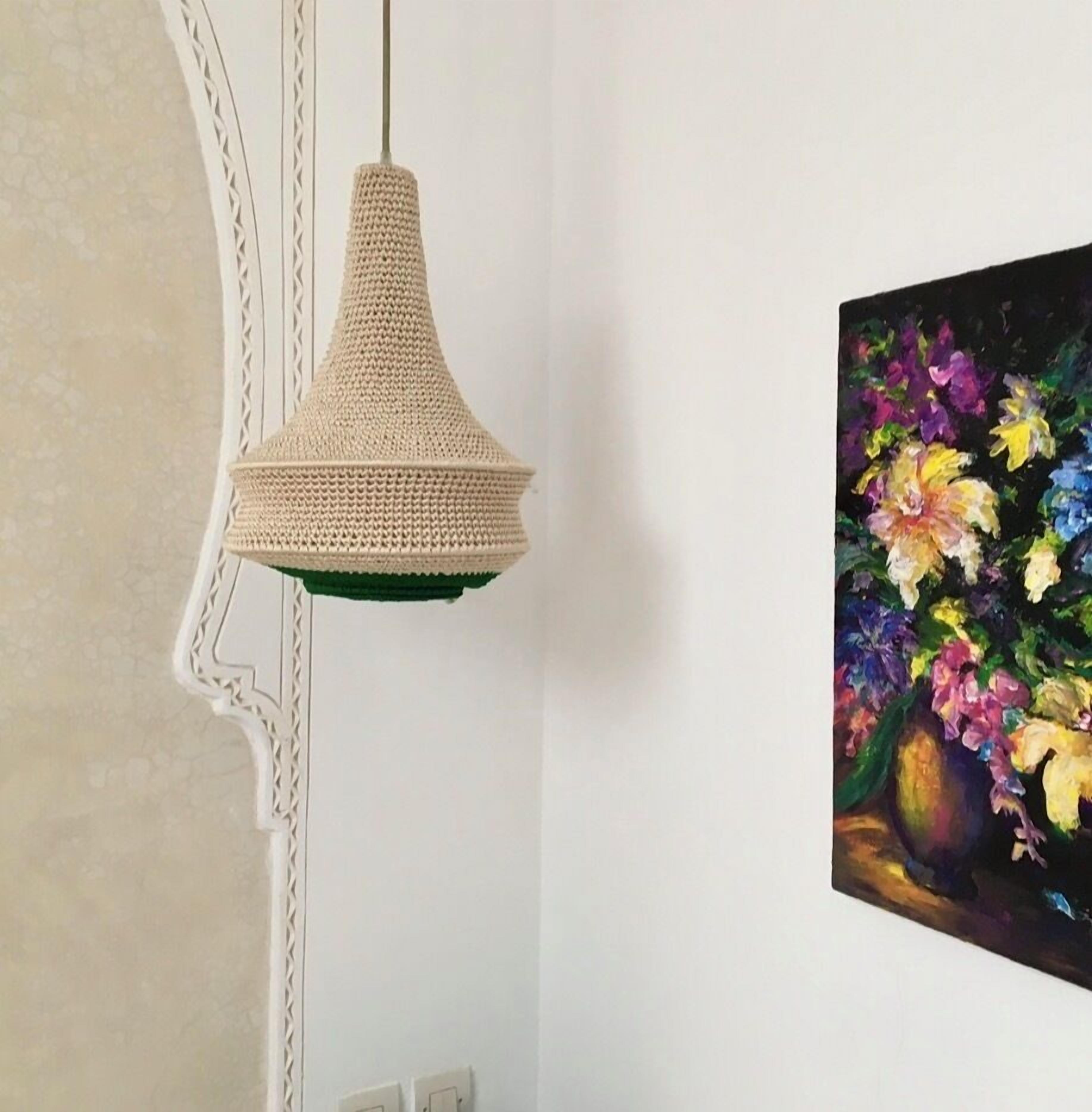 Une pièce avec un luminaire suspendu en fibres tressées, un mur blanc et un tableau représentant des fleurs.