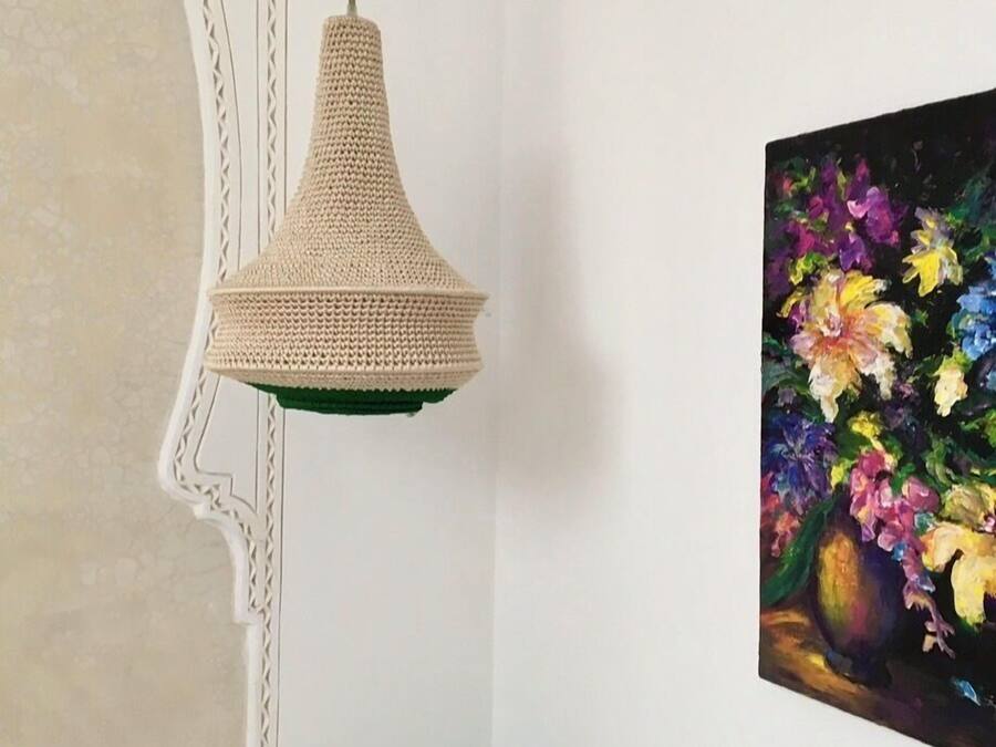 Une pièce avec un luminaire suspendu en fibres tressées, un mur blanc et un tableau représentant des fleurs.