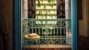 An arched doorway leading to a balcony with a wrought iron railing, a hanging lantern, and a chair with a book. - Riad Lumière (Marrakech)