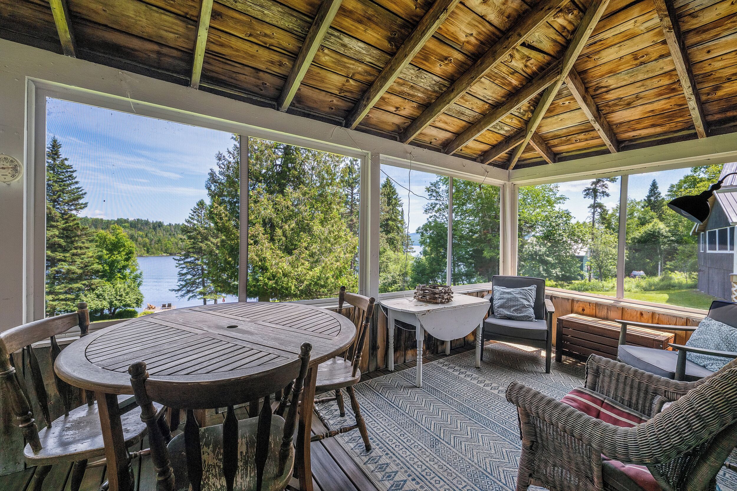A covered outdoor area with a table and chairs, a bench, and a view of a lake and forest.