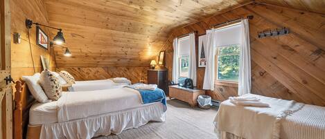 Ein gemütliches Schlafzimmer im Blockhausstil mit zwei Betten, einer Holzbalkendecke und Blick ins Grüne.